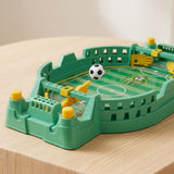 Green tabletop soccer game on a wooden table with a black-and-white ball suspended just above the yellow launcher.