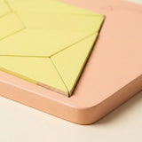 A geometric puzzle close-up shows pale yellow wooden pieces with exposed wood edges inside a peach tray with a rounded corner.