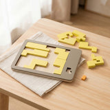 A wooden geometric puzzle has yellow interlocking pieces inside and around a grey tray on cream fabric over a light wooden table.