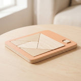 Cream wooden geometric puzzle pieces fitted into a peach board with layered edges, on a light wooden table beside a window.