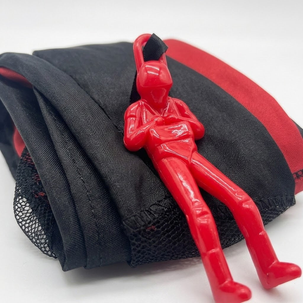 Red plastic soldier rests on the parachute toy’s folded red and black canopy with mesh edging against a white background.