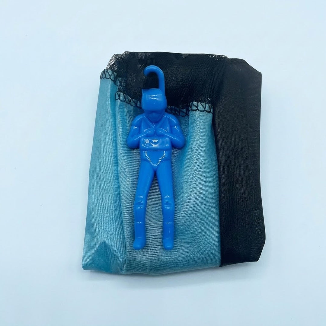 Blue parachute toy has a plastic soldier resting on its folded blue and black canopy against a pale blue background.