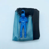 Blue parachute toy has a plastic soldier resting on its folded blue and black canopy against a pale blue background.