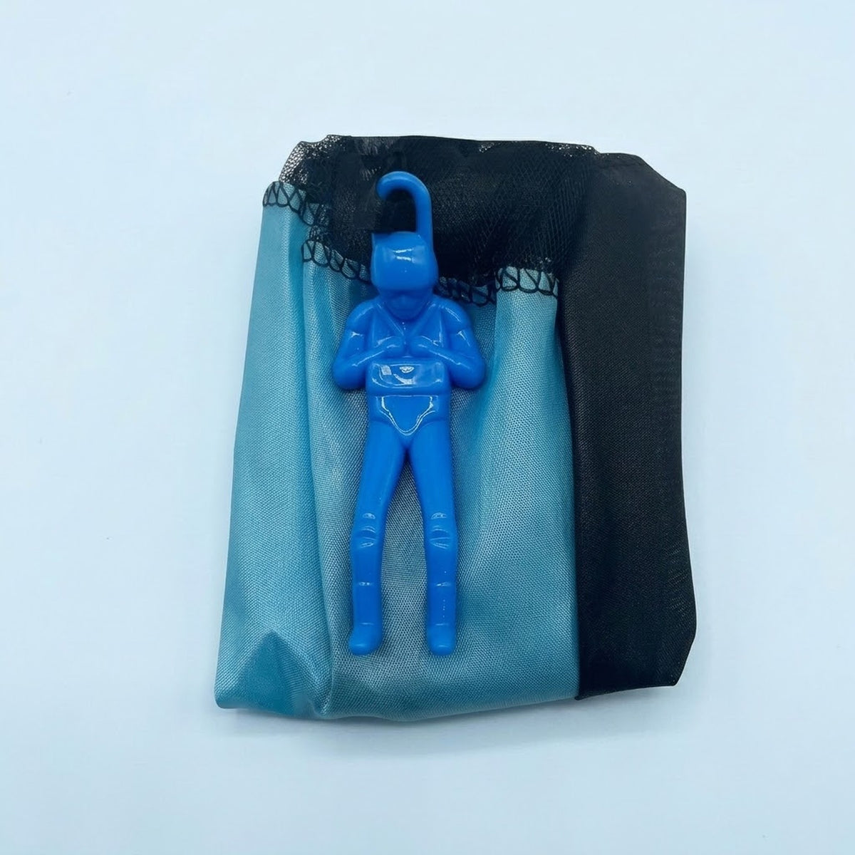 Blue parachute toy has a plastic soldier resting on its folded blue and black canopy against a pale blue background.