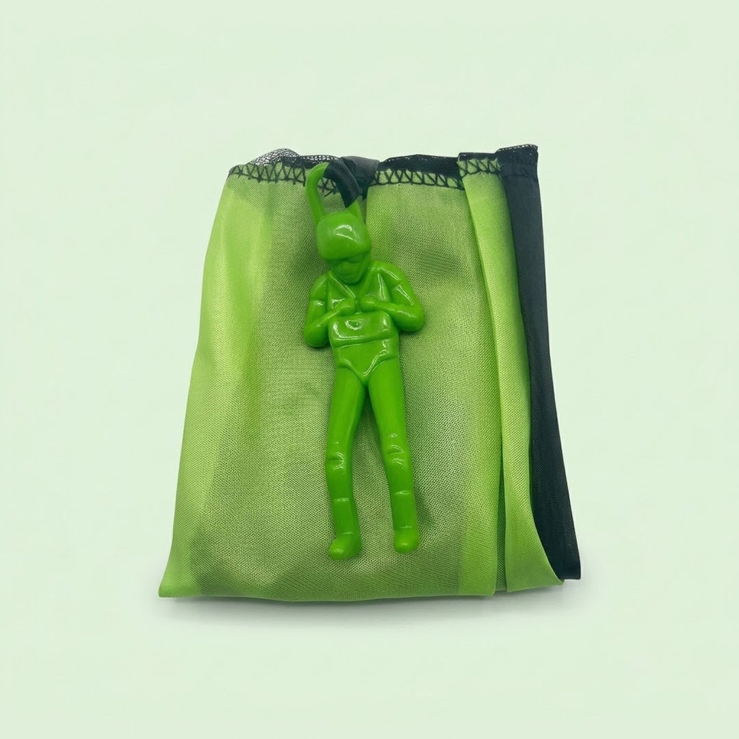 Folded green parachute toy with its green plastic soldier figure on top, photographed against a plain pale green background.