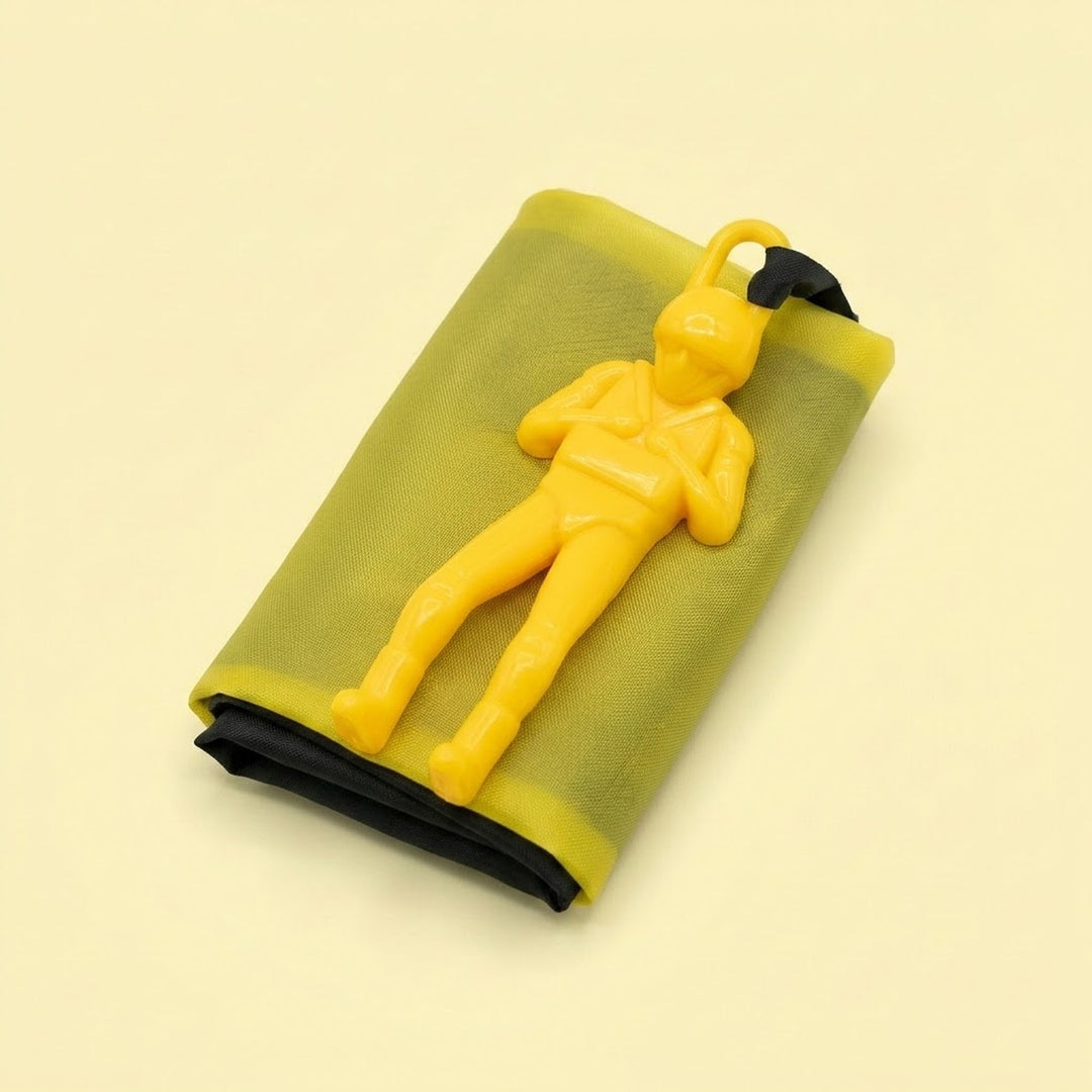 Yellow parachute toy has a plastic soldier resting on its folded yellow canopy with black edging against a pale yellow background.