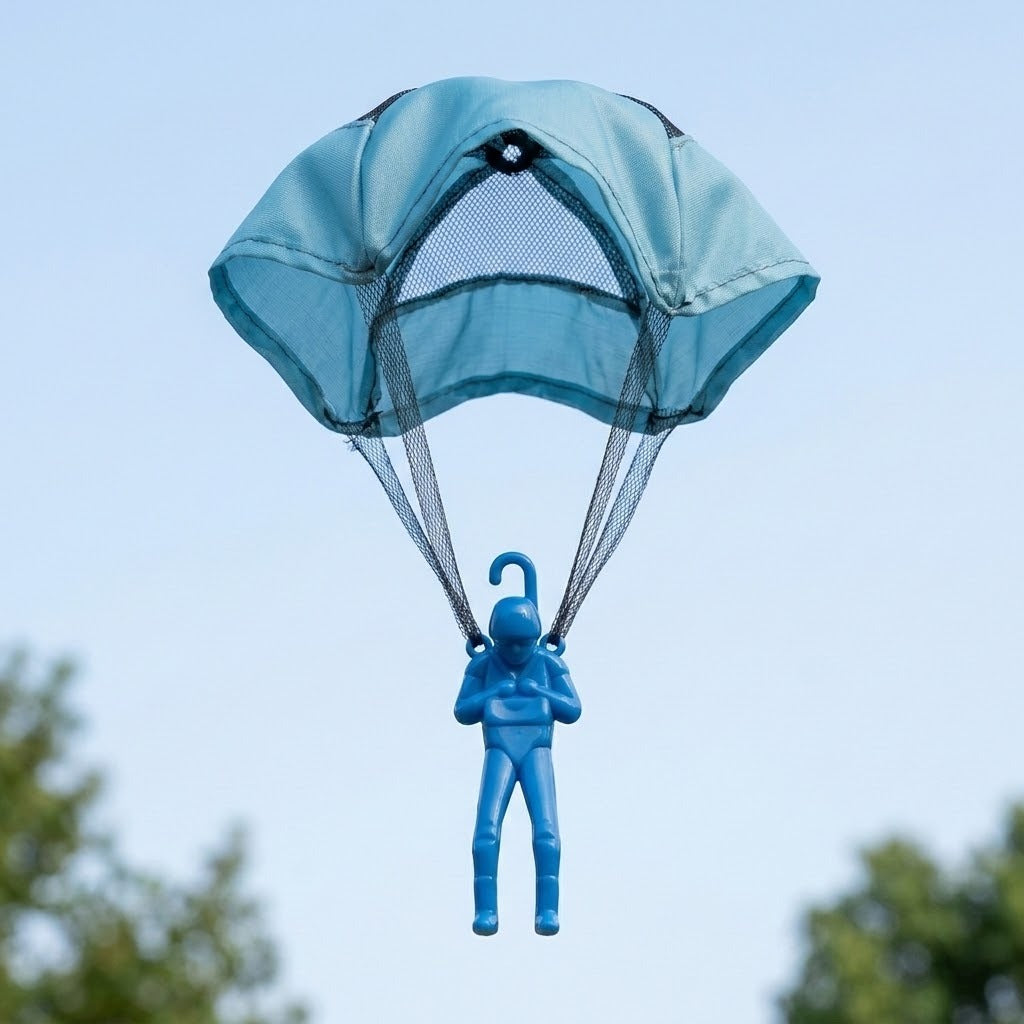 Light blue toy parachute carrying a blue plastic soldier figure, flying against a pale blue sky with blurred green foliage below.