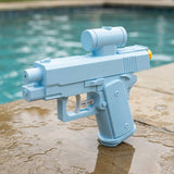 Light blue water squirt gun with a cylindrical upper reservoir stands on wet paving beside a turquoise swimming pool.