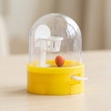 A yellow plastic mini basketball game with a clear dome, white hoop and orange ball sits on a beige tabletop.