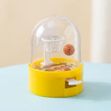 A yellow mini basketball game shows an orange ball suspended beside its white hoop above a pale blue surface.