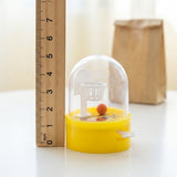 A yellow mini basketball game stands beside a wooden ruler marked zero through seven, with a brown paper bag behind.