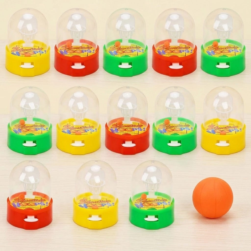 Mini plastic basketball games with clear domes and red, yellow, or green bases stand beside an orange ball on a cream background.