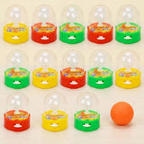 Mini plastic basketball games with clear domes and red, yellow, or green bases stand beside an orange ball on a cream background.
