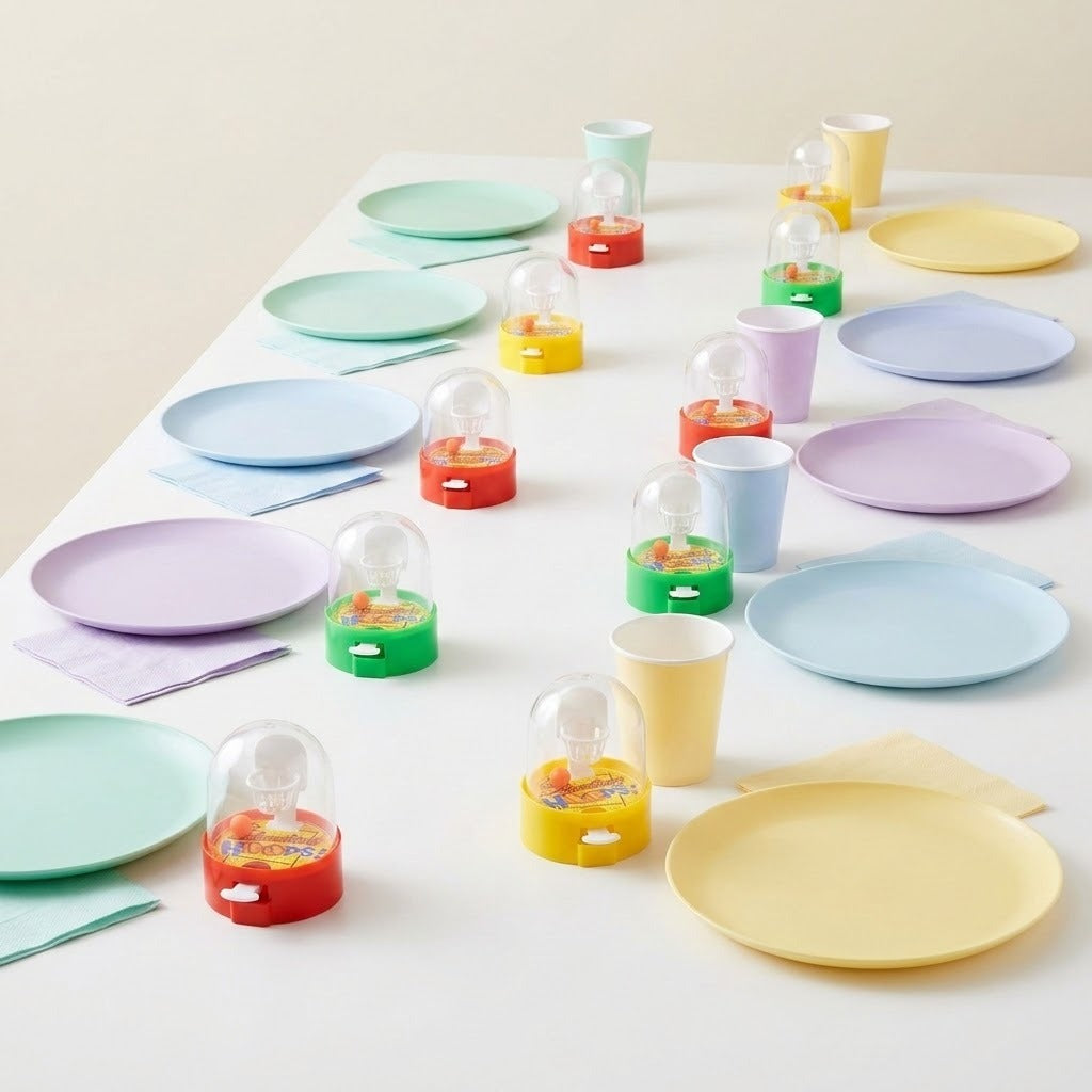 Red, yellow and green mini basketball games sit individually beside pastel plates, cups and napkins on a white party table.