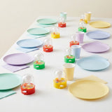 Red, yellow and green mini basketball games sit individually beside pastel plates, cups and napkins on a white party table.