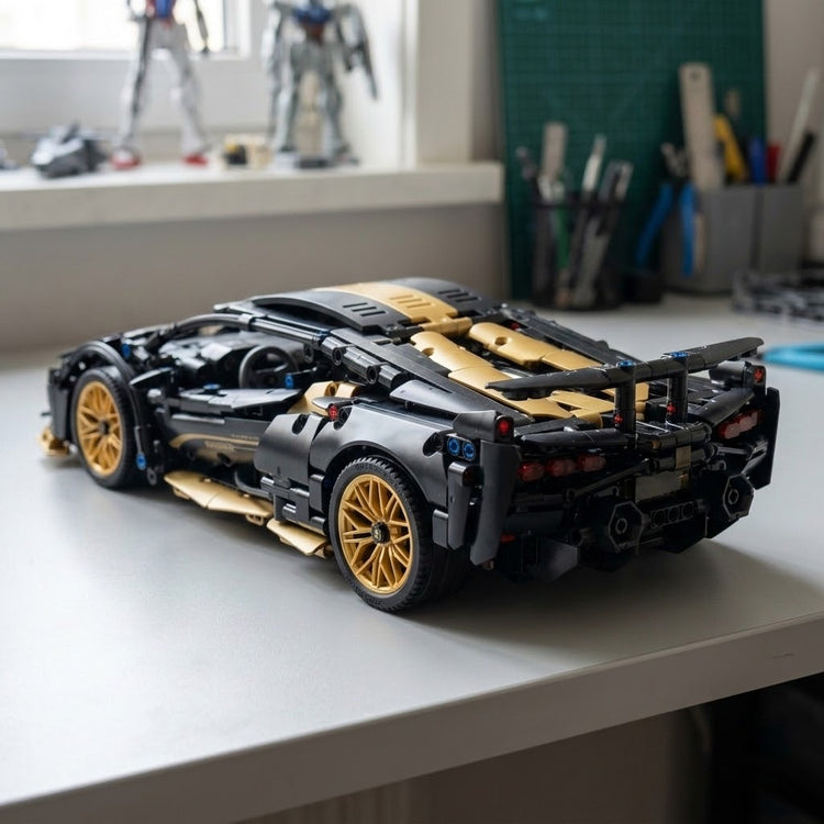 An assembled black and gold car building kit sits on a white desk, showing gold wheels and a rear spoiler against blurred workshop tools.