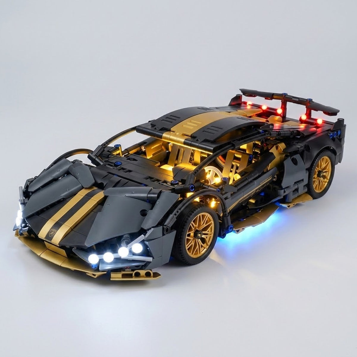 Assembled black and gold car building kit has gold wheels, glowing cabin lights, and a rear spoiler against a light gray background.