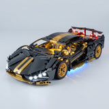 Assembled black and gold car building kit features illuminated headlights, cabin lights, and blue underglow on a light gray background.