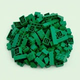 Dark green plastic building blocks form a broad pile with raised studs and hollow undersides visible against a pale mint background.