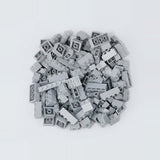 Light gray plastic building blocks in assorted sizes form a compact pile on a pale gray background.