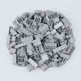 Light gray plastic building blocks form a broad pile with raised studs and hollow undersides visible on a pale gray background.