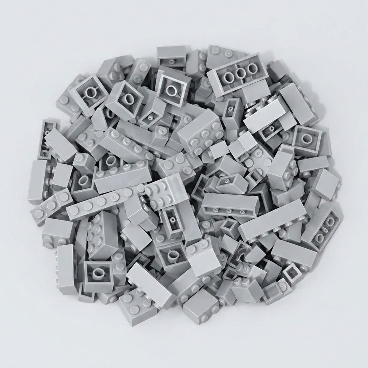 Light gray plastic building blocks form a broad pile with raised studs and hollow undersides visible on a pale gray background.
