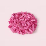 Pink plastic building blocks in assorted rectangular sizes form a compact pile on a pale pink background.