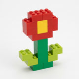 Building blocks form an upright flower with red petals, a yellow center, and green stem and leaves against a white background.