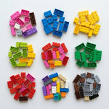 Colorful building blocks are arranged in nine small groups across three rows on a white surface, loosely sorted by color.