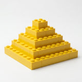 Yellow interlocking building blocks form a stepped square pyramid on a white surface against a white background.