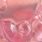 A close-up of a translucent pink resin miniature figurine reveals glossy curled details and tiny surface marks.