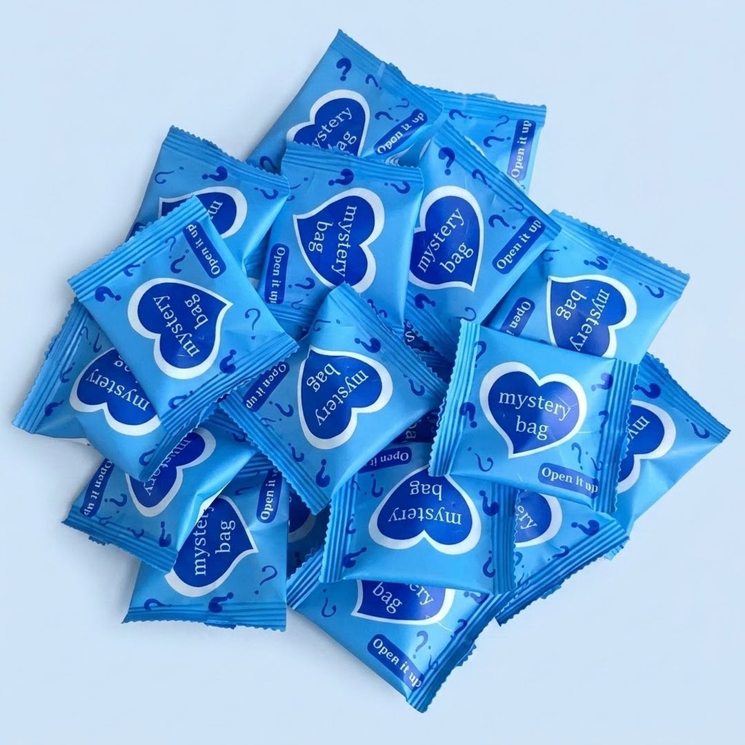 Blind bags for resin miniature figurines form a loose mound on pale blue, their blue wrappers decorated with hearts and question marks.