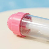 A close-up shows the pink nozzle, clear plastic barrel, and white inner tube of a water gun on a beige surface.