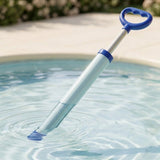 A blue and clear plastic water gun sits diagonally in pool water with its white plunger extended and loop handle raised.