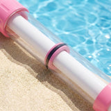 Close-up of a pink and clear water gun with a white inner tube lying on sand beside a swimming pool.