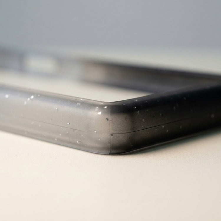 Close-up of a translucent black-gray slab bumper corner shows pale speckles and a recessed edge on a light surface.