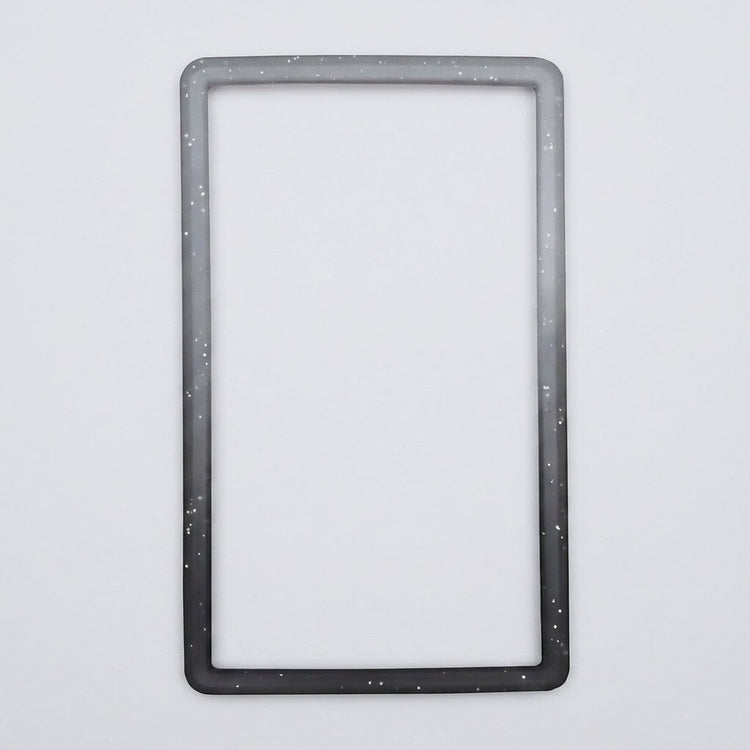 A speckled gray-to-black silicone TPU slab bumper lies flat on a light gray background with its open center visible.
