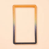 An orange-to-black silicone TPU slab bumper with white speckles lies flat on a pale peach background.
