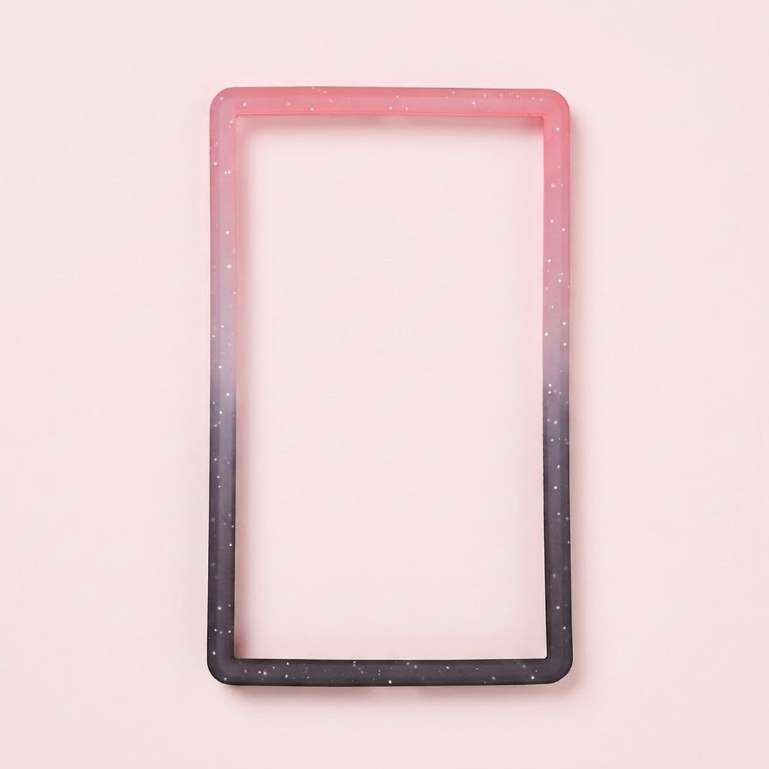 A pink-to-black silicone TPU slab bumper with white speckles lies flat on a pale pink background.