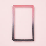A pink-to-black silicone TPU slab bumper with white speckles lies flat on a pale pink background.
