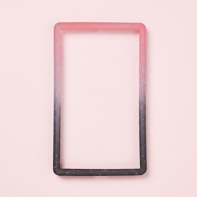 A pink-to-black silicone TPU slab bumper with white speckles lies flat on a pale pink background.
