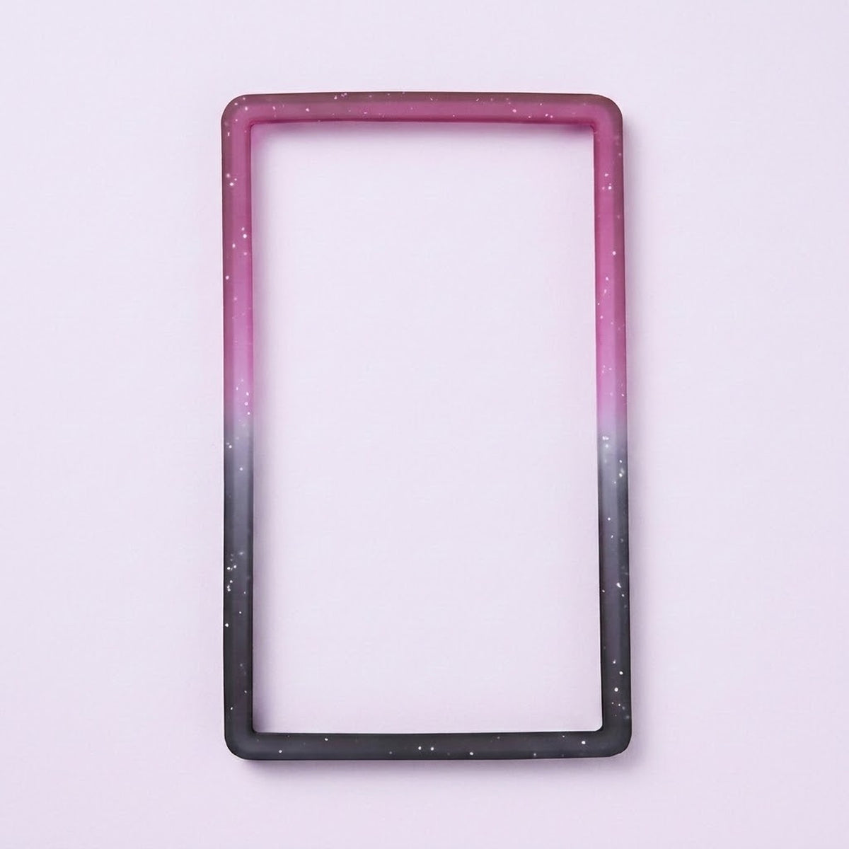 A purple-to-black silicone TPU slab bumper with white speckles lies flat on a pale lavender background.