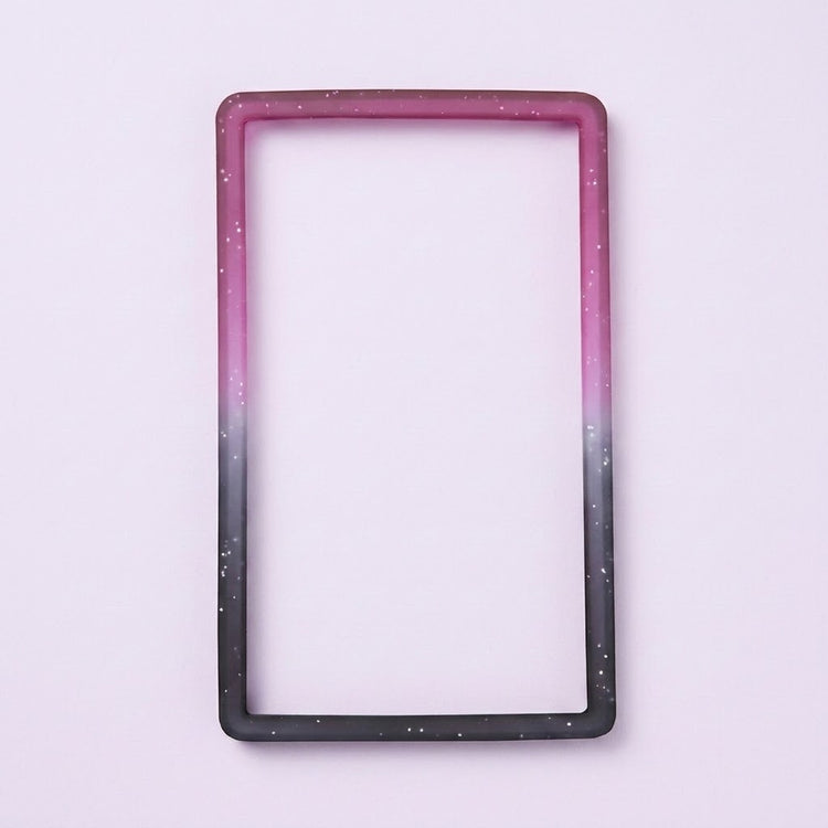 A purple-to-black silicone TPU slab bumper with white speckles lies flat on a pale lavender background.