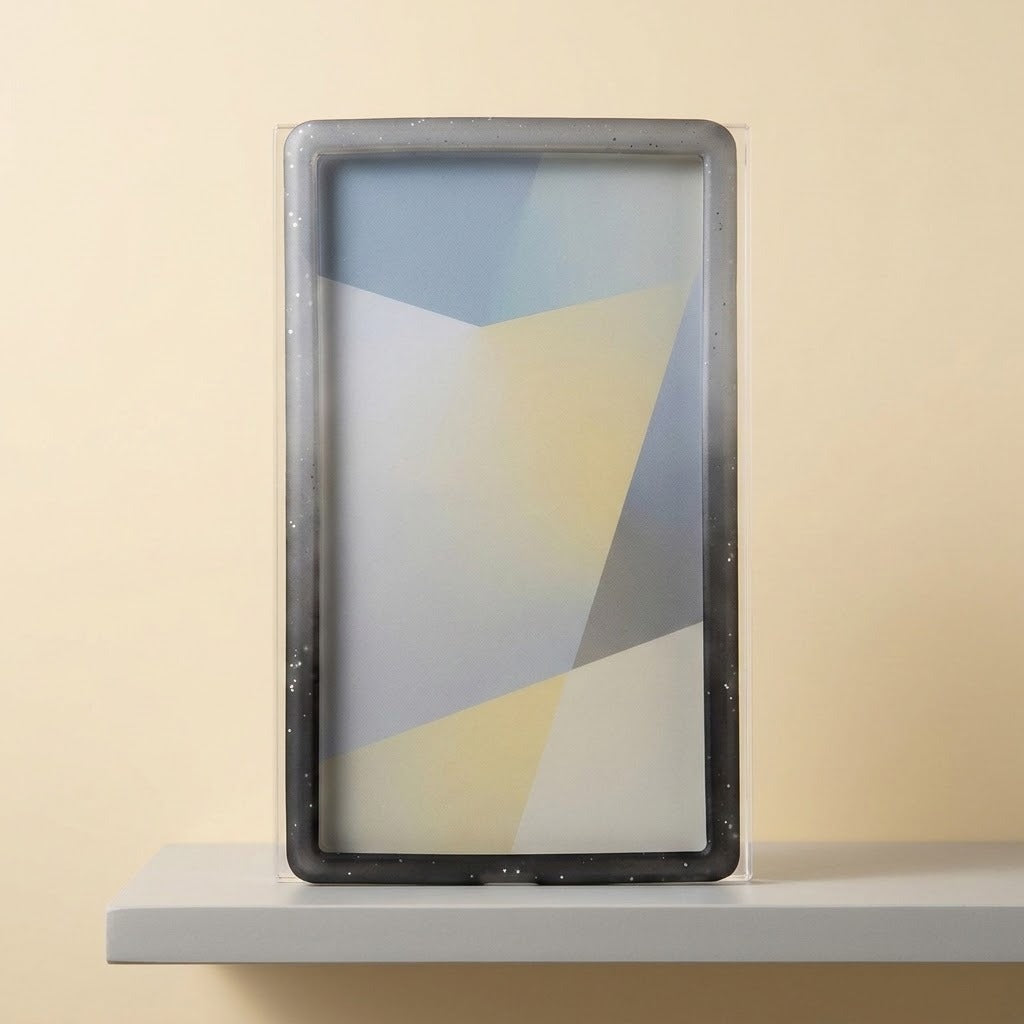 A speckled gray-to-black slab bumper surrounds a clear slab with a geometric insert, standing on a white shelf against a beige wall.