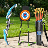A toy bow and arrow set displayed outdoors on a stone patio with grass and flowers in the background. The set includes a blue and gray bow, a black target stand with an orange and white target, a black quiver holding orange arrows with gold tips, and a Super Archery logo on the quiver.