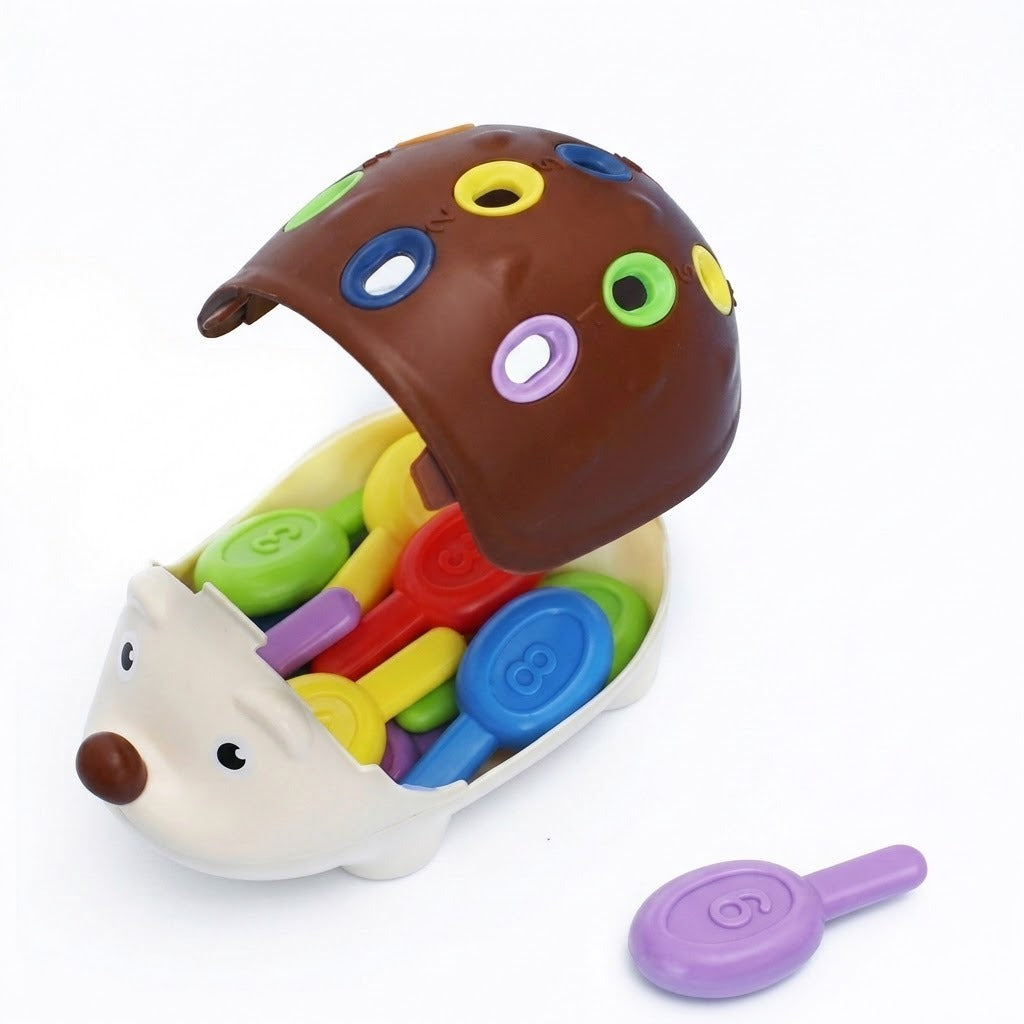 Cream hedgehog sensory toy has a raised brown shell, colorful pegs inside, and a loose purple peg on a white background.