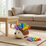 Brown and cream hedgehog sensory toy with colorful plastic pegs sits on a woven rug beside loose pegs, with a sofa behind.