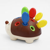 A plastic hedgehog-shaped sensory toy with a brown back, cream-colored head and legs, and colorful peg holes and spikes in blue, green, red, and yellow on a white background.