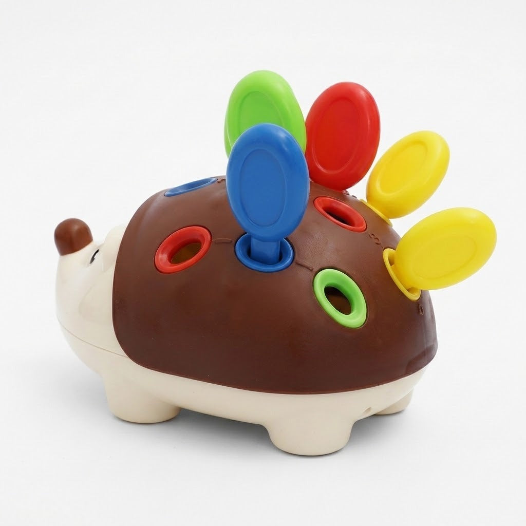 A plastic hedgehog-shaped sensory toy with a brown back, cream-colored head and legs, and colorful peg holes and spikes in blue, green, red, and yellow on a white background.