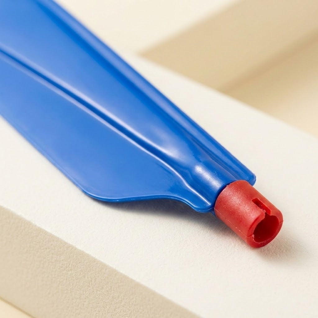 A balloon helicopter set's blue plastic propeller blade has a red connector, shown close up on a light beige surface.